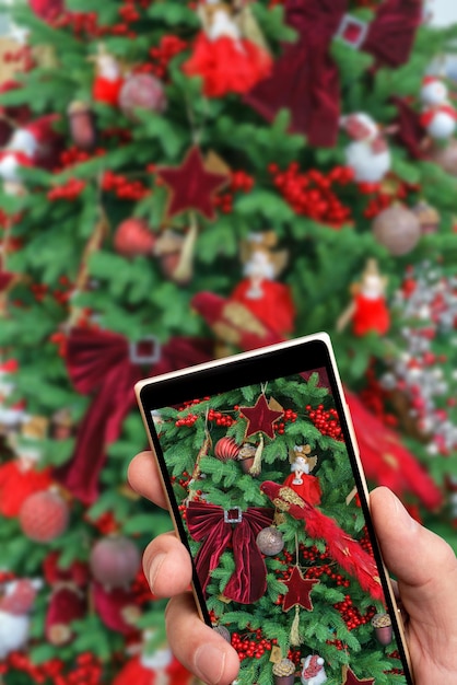 Décorations rouges sur les branches d'un sapin de Noël vert sur l'écran du smartphone Fond festif