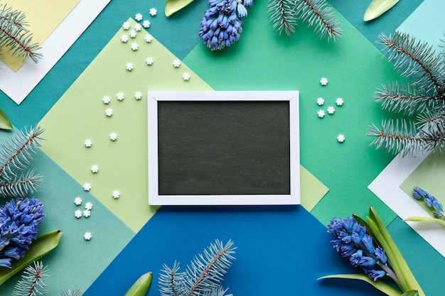 Décorations saisonnières d'hiver autour d'un tableau noir avec un espace pour le texte Fond de papier géométrique en couches vert avec des fleurs de jacinthe fraîches naturelles bleues et des brindilles de sapin