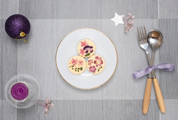 Décorations de table de Noël avec une assiette de biscuits aux fleurs comestibles et bougie parfumée.