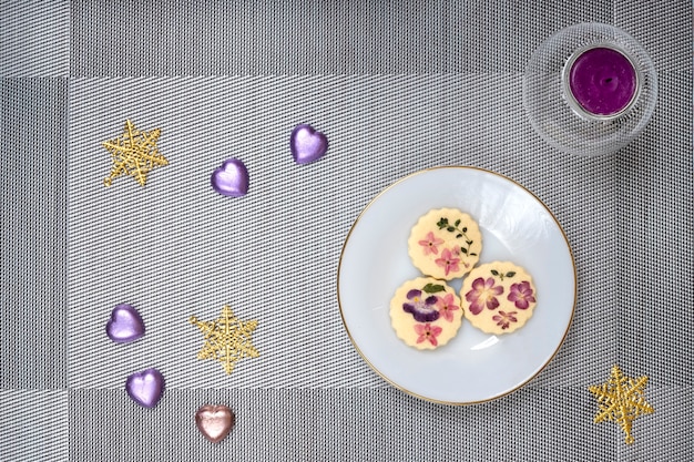 Décorations de table de Noël avec une assiette de biscuits aux fleurs comestibles et bougie parfumée.