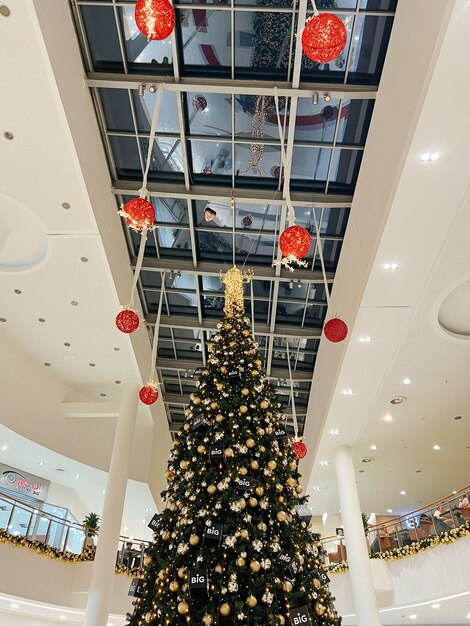 Décoré de boules et de guirlandes, un grand arbre de noël se dresse dans un centre commercial entre les étages