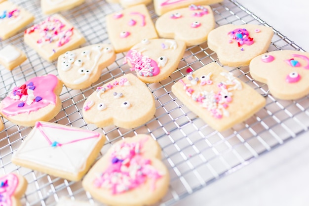 Décorer des biscuits au sucre en forme de coeur avec du glaçage royal et des paillettes roses pour la Saint-Valentin.