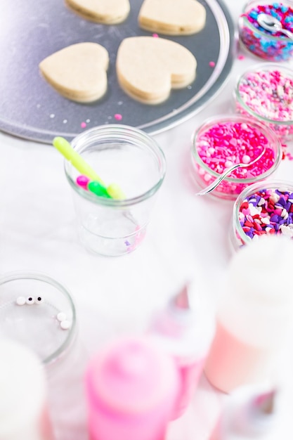 Décorer des biscuits au sucre en forme de coeur avec du glaçage royal et des paillettes roses pour la Saint-Valentin.