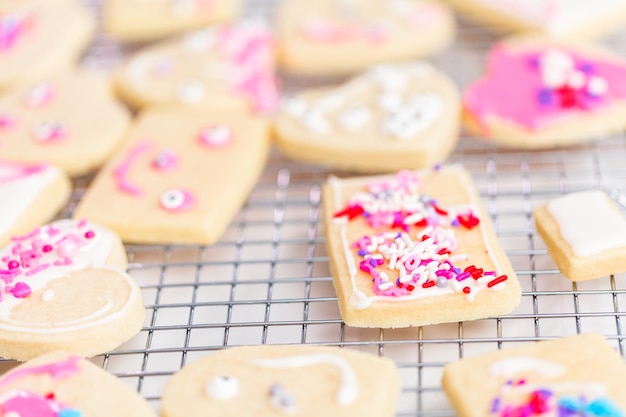 Décorer des biscuits au sucre en forme de coeur avec du glaçage royal et des paillettes roses pour la Saint-Valentin.