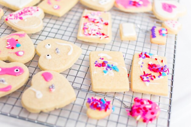 Décorer des biscuits au sucre en forme de coeur avec du glaçage royal et des pépites roses pour la Saint-Valentin.