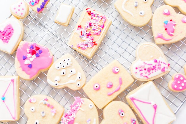 Décorer des biscuits au sucre en forme de coeur avec du glaçage royal et des pépites roses pour la Saint-Valentin.