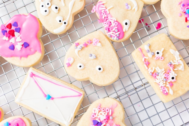 Décorer des biscuits au sucre en forme de coeur avec du glaçage royal et des pépites roses pour la Saint-Valentin.