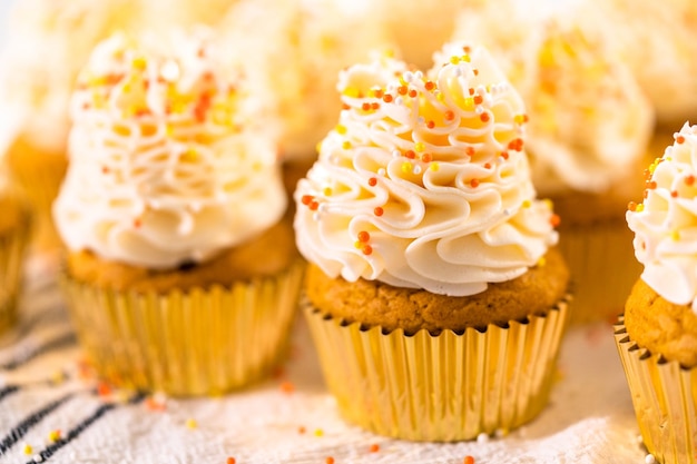 Décorer un cupcake aux épices à la citrouille avec de la crème au beurre italienne et des vermicelles.