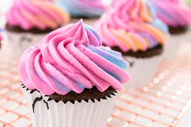 Décorer des cupcakes de licorne au chocolat avec du glaçage au beurre coloré et des vermicelles.