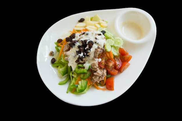 Découpe de salade de thon avec légumes mélangés sur plaque blanche sur fond noir isolé.