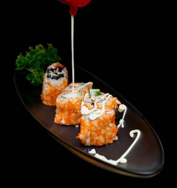 Découpe de Sushi roll cuisine japonaise avec caviar et mayonnaise gros plan sur fond noir isolé