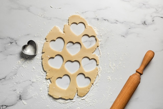 Découper des biscuits en forme de coeur à partir de pâte sablée étalée sur une table en marbre saupoudrée de farine rouleau à pâtisserie vue de dessus Cuisson pour la Saint-Valentin