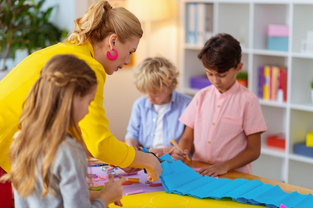 Découpez du papier bleu. Enseignant portant une veste jaune aidant les élèves à couper du papier bleu pour l'ornement appliqué