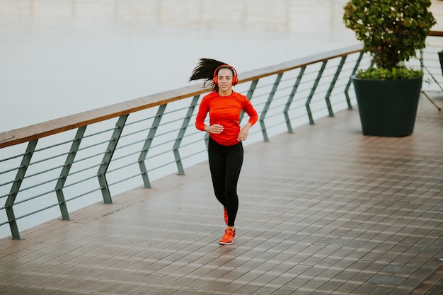 Découvre à active belle jeune femme qui court sur la promenade le long du fleuve