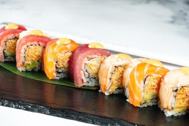 Photo définissez des rouleaux de sushi servis sur une feuille de bananier sur une pierre noire sur une table en marbre avec des baguettes et de la sauce de soja. nourriture japonaise. sushi de saumon et de crevettes au thon. fruits de mer sains.