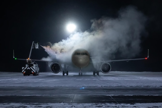 Dégivrage au sol d'un avion de passagers sur l'aire de trafic nocturne de l'aéroport en hiver