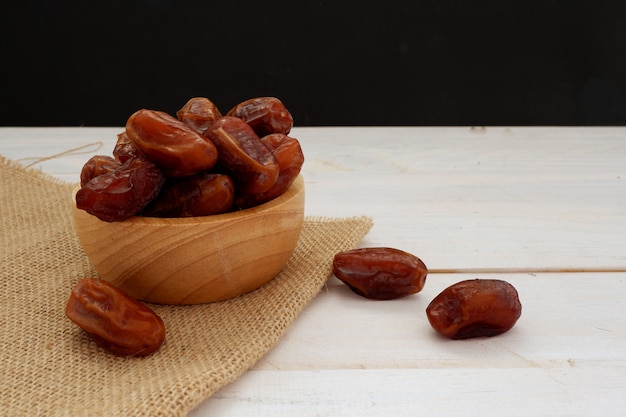 Deglet nour dates dans un bol en bois sur fond de bois blanc