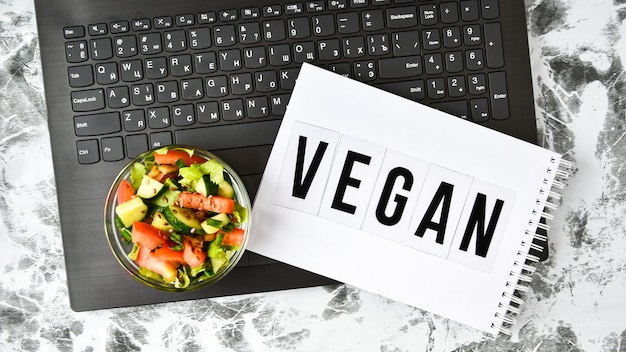 Déjeuner d'affaires sain au bureau, salade de légumes, mot VEGAN sur ordinateur portable avec stylo