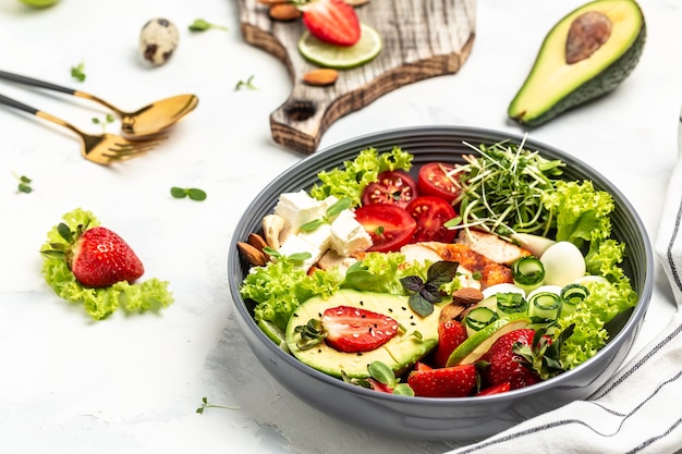 Déjeuner de bol de bouddha de légumes sains avec poulet grillé et avocat, fromage feta, œufs de caille, fraises, noix et laitue sur fond blanc. Vue de dessus.