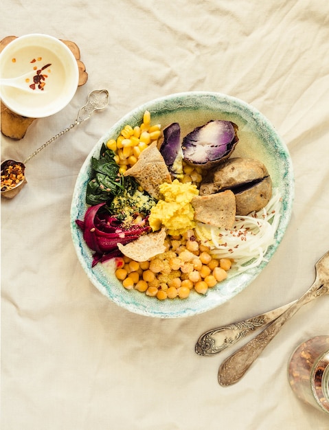 Déjeuner de désintoxication végétalien avec une pomme de terre violette, des épinards cuits et du houmous avec des craquelins de maïs.