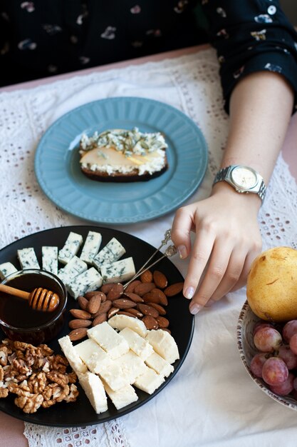 Un déjeuner gourmand: une assiette noire d'apéritifs sur une nappe blanche: noix, amandes, fromage, roquefort