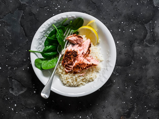 Déjeuner méditerranéen sain couscous au citron saumon grillé et épinards frais sur fond sombre vue de dessus