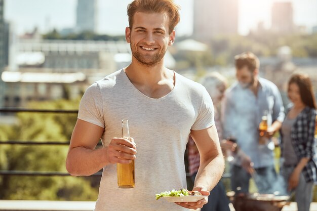 Déjeuner parfait avec des amis jeune et bel homme tient une bouteille de bière et une assiette