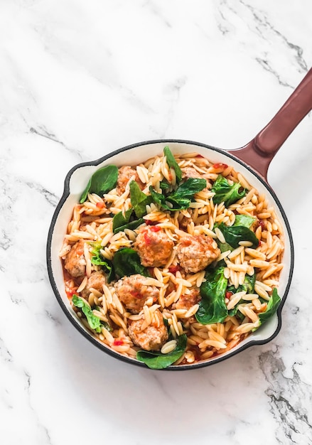 Un déjeuner en pot Pâtes Orzo avec boulettes de viande et épinards à la sauce tomate dans une poêle à frire sur fond clair vue de dessus