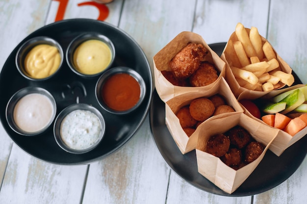 Déjeuner de restauration rapide dans plusieurs emballages différents types de restauration rapide et de malbouffe à côté d'un bol noir avec cinq types de sauce différents