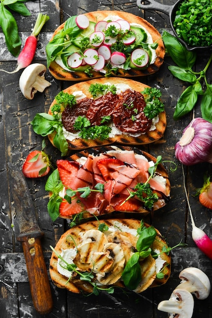 Déjeuner Sandwichs faits maison avec tomates, prosciutto, légumes et fromage sur fond de pierre noire Bruschetta Vue de dessus