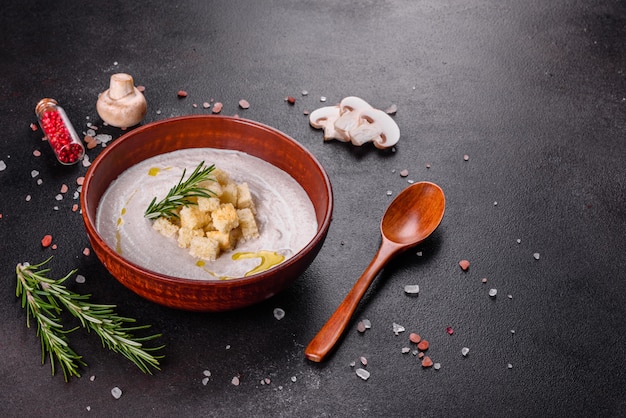 Délicieuse belle soupe aux champignons dans une assiette brune avec une cuillère en bois sur un fond brun foncé