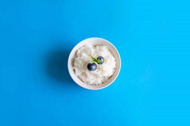 Photo délicieuse bouillie de riz aux bleuets dans un bol blanc sur fond bleu. concept de petit déjeuner sain et sain