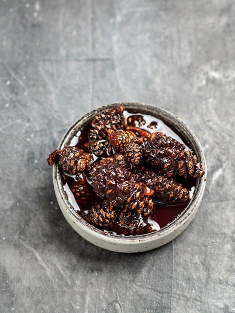 Délicieuse confiture de pommes de pin dans un petit bol. Dessert sibérien traditionnel avec de la confiture de pommes de pin jeunes sur la texture grise