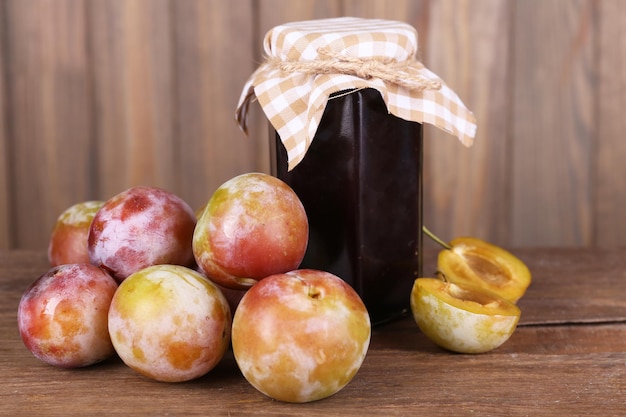 Photo une délicieuse confiture de prunes dans un pot et des prunes sur une table en bois sur un fond en bois