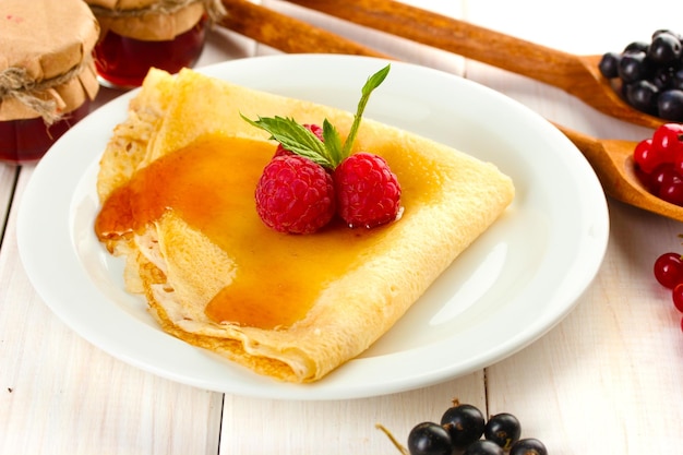 Délicieuse crêpe aux fruits rouges et miel sur plaque sur table en bois