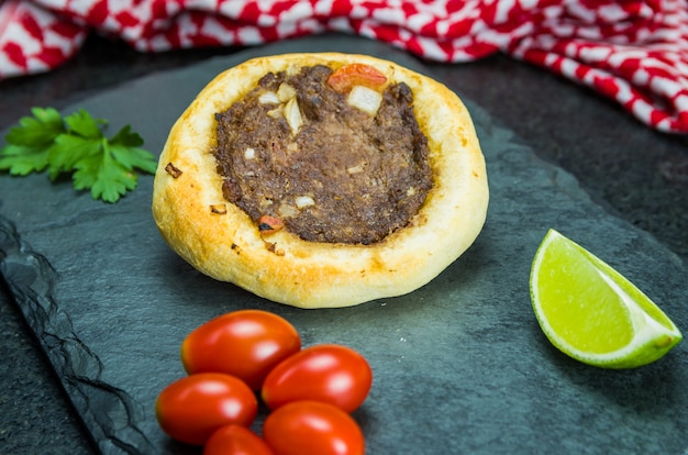 Délicieuse cuisine libanaise, sfihas légitimes sur fond de granit noir avec des tomates, des citrons avec Keffieh en arrière-plan.