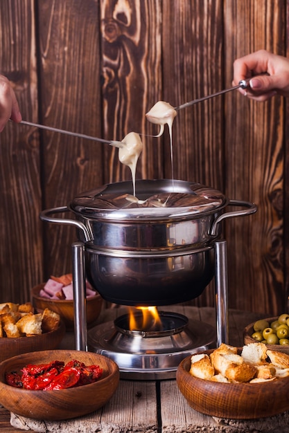 Photo délicieuse fondue au fromage sur une fourchette sur un support en bois