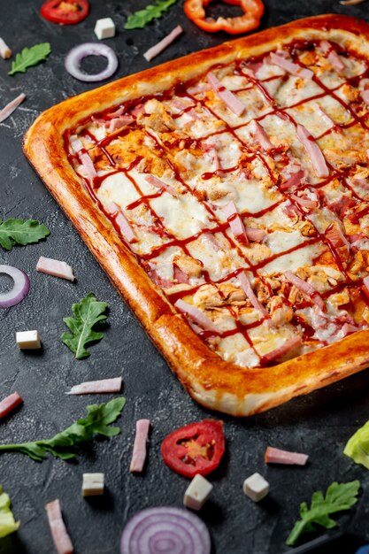 Une délicieuse pizza au pain plat à croûte carrée avec bacon et fromage. Pizza italienne fraîche maison Margherita aux olives et poivrons rouges sur fond sombre