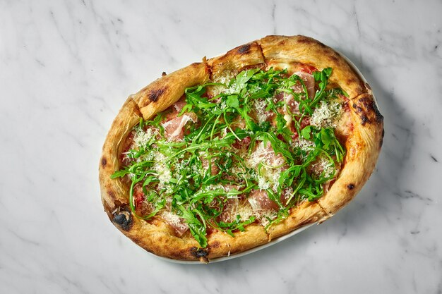 Délicieuse pizza au prosciutto, sauce tomate, parmesan et roquette sur plaque blanche sur marbre blanc