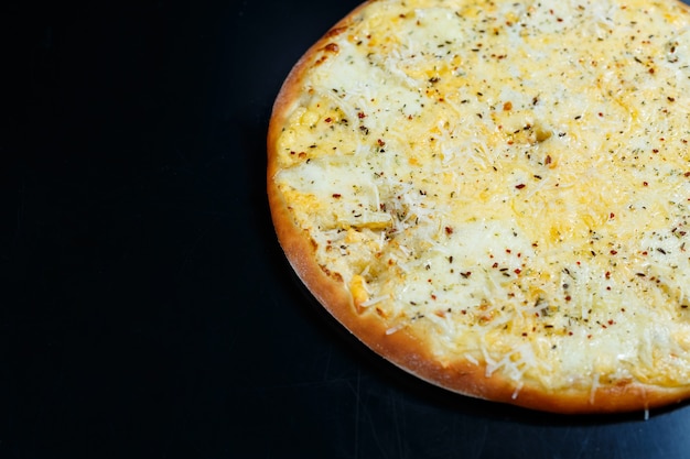 Délicieuse pizza aux quatre fromages avec cheddar, parmesan, mozzarella et sauce tomate sur fond noir. Vue d'en-haut.