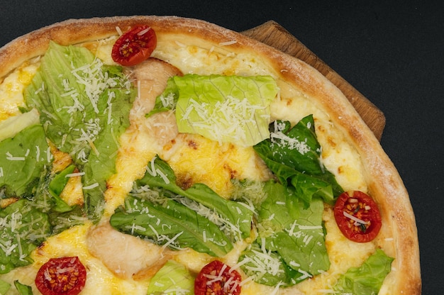 Délicieuse pizza cesar fraîche avec du poulet et des légumes sur une planche de bois sur une surface noire