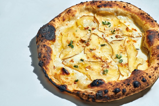 Photo délicieuse pizza italienne au feu de bois avec sauce crémeuse, noix de cajou, poire, mozzarella et gorgonzola sur une surface grise. lumière forte.