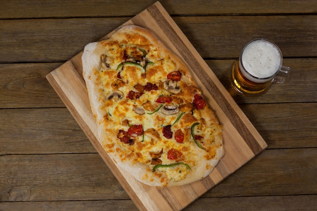 Délicieuse pizza servie sur plateau à pizza avec un verre de bière sur une planche en bois