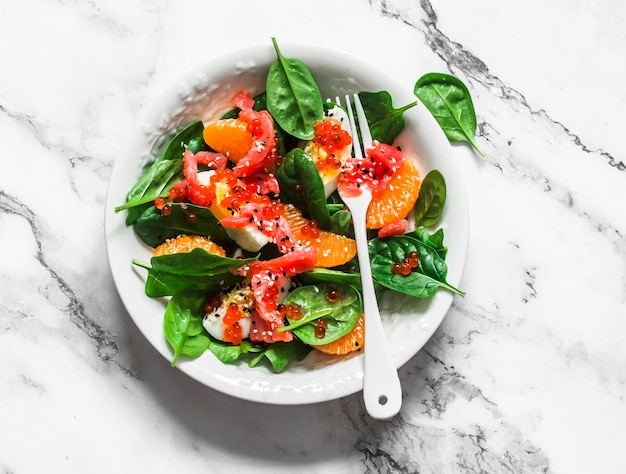 Délicieuse salade aux épinards oeuf bouilli saumon mandarine et caviar rouge avec vinaigrette aux agrumes sur fond clair vue de dessus