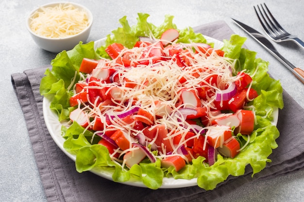 Une délicieuse salade de bâtonnets de crabe aux tomates cerises et au fromage râpé avec des oignons dans un plat de service.