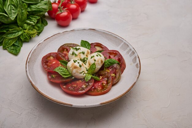 Délicieuse salade caprese avec tomates rouges, basilic frais et fromage mozzarella dans une assiette blanche en gros plan