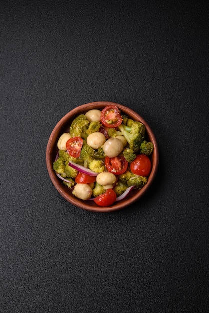 Délicieuse salade fraîche avec brocoli tomates cerises champignons oignons sel épices et herbes sur fond de béton foncé