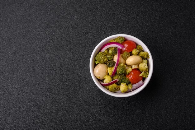 Délicieuse salade fraîche avec brocoli tomates cerises champignons oignons sel épices et herbes sur fond de béton foncé