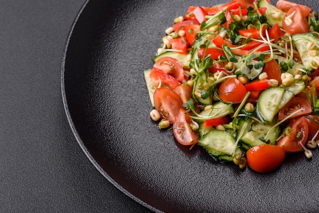 Délicieuse salade fraîche juteuse de tomates poivrons concombre microgreens et haricot mungo germé sur une plaque en céramique noire sur un fond de béton foncé