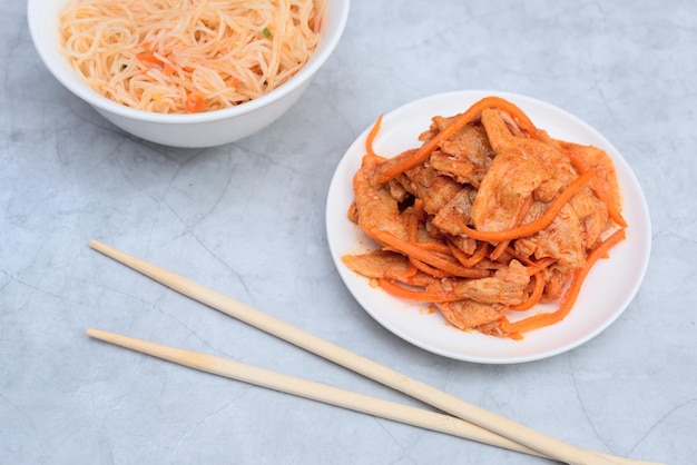 Délicieuse salade funchose asiatique et salade de viande végétalienne au soja dans des bols blancs avec des bâtons de bois sur fond gris Mise au point sélective Concept de cuisine asiatique